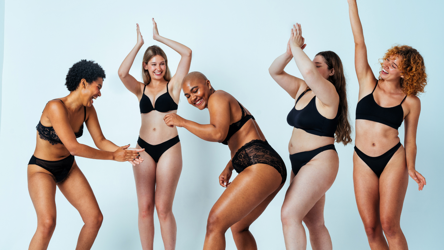 Five women of different body types wearing black lingerie against a light blue background